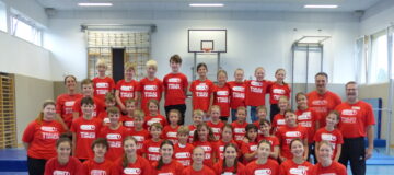 Eine Gruppe von Burschen und Mädchen in roten Union-T-Shirts, die in einer Turnhalle stehen
