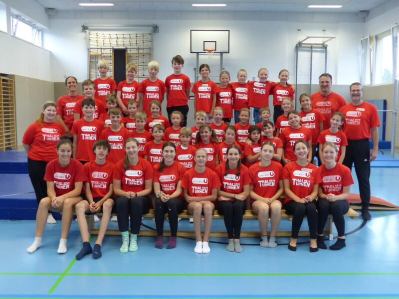 Eine Gruppe von Burschen und Mädchen in roten Union-T-Shirts, die in einer Turnhalle stehen